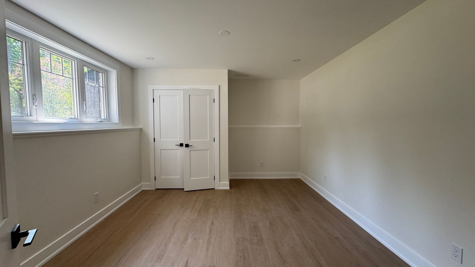 Empty beige room with wood floor, white closet doors, and a window letting in daylight.