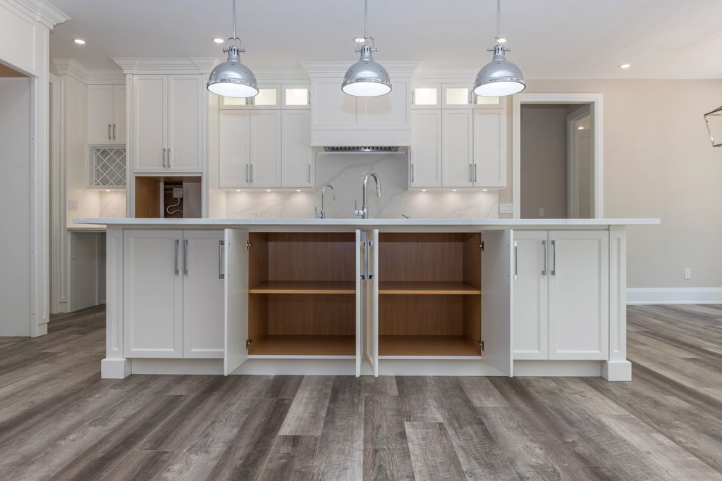 Bright modern kitchen with white cabinets, large island, pendant lights, and wood-look flooring