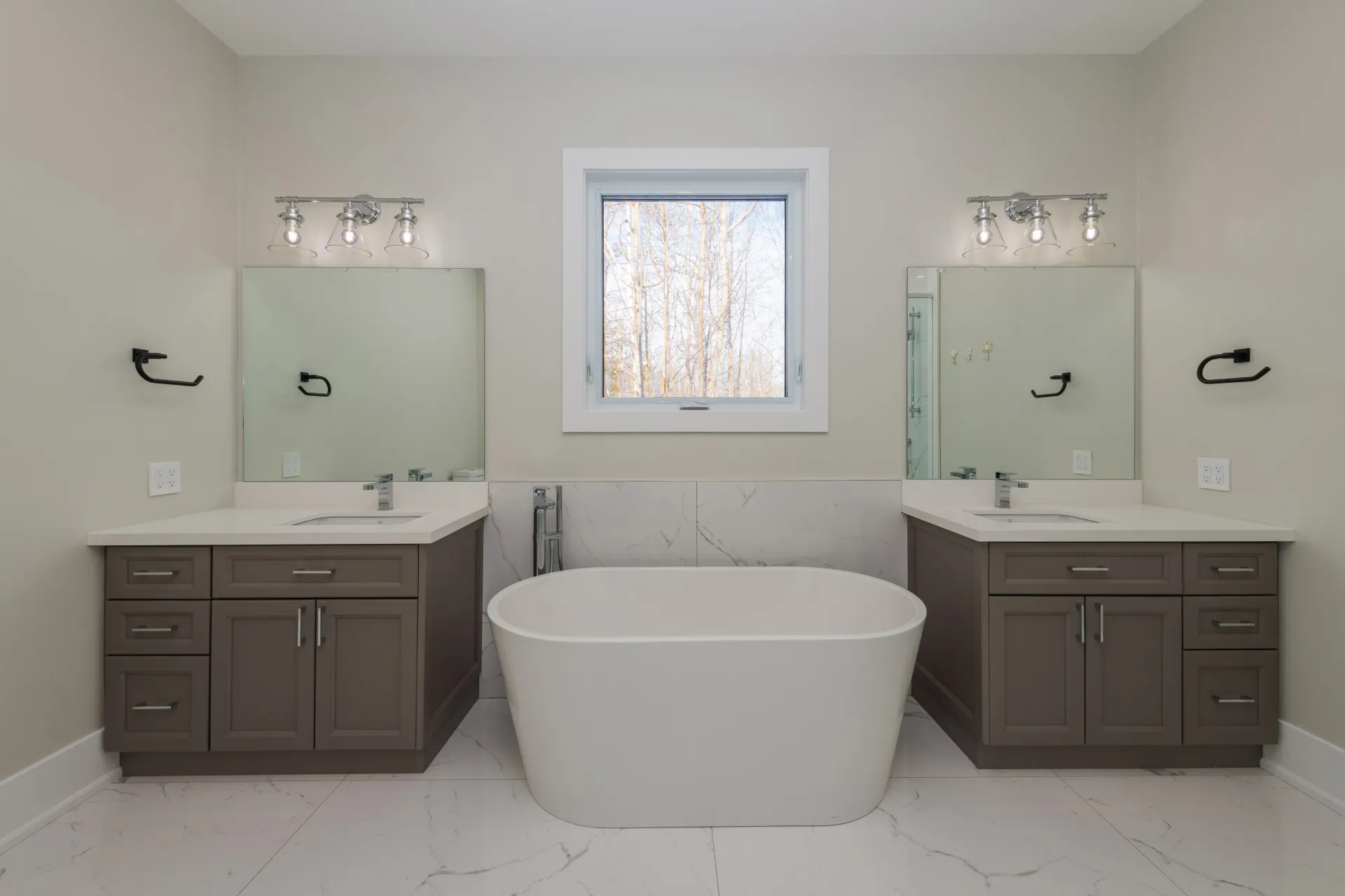 Modern bathroom featuring a central freestanding tub between two gray double vanities with white countertops and mirrors.