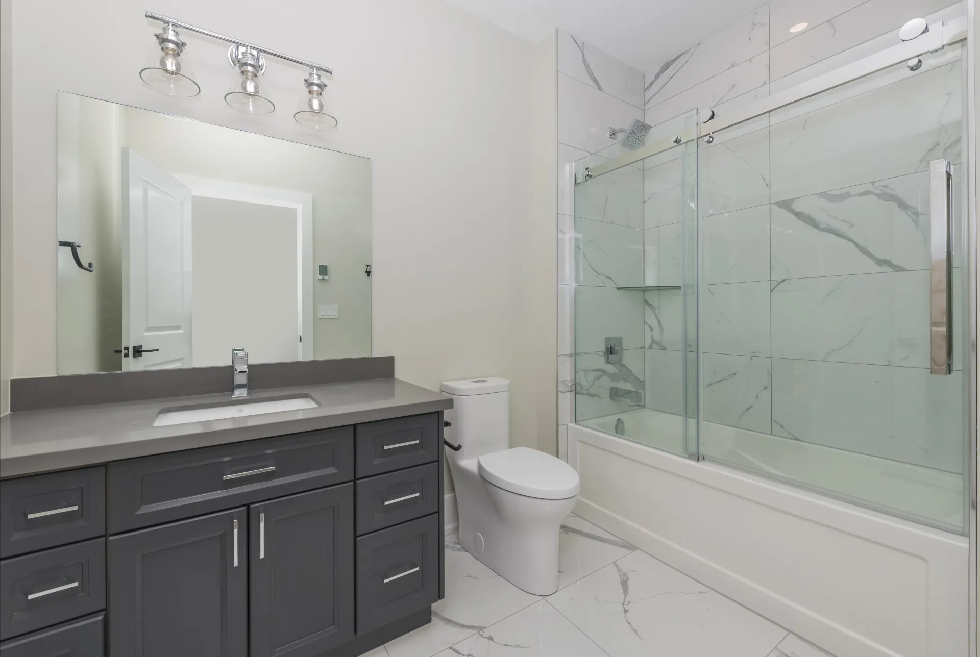 Modern bathroom with dark grey vanity, white marble tile shower, glass door, and a white toilet.