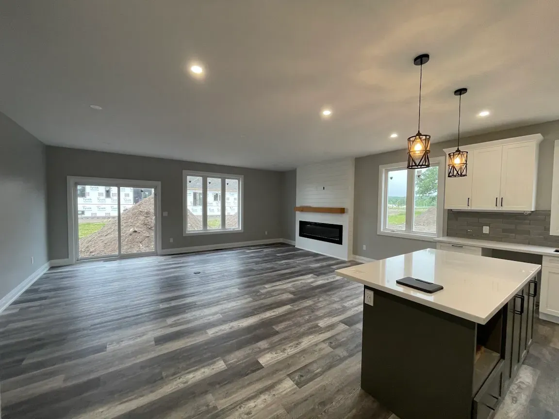 Modern open-concept living area with gray wood floors, white kitchen cabinets, a center island, and a fireplace.