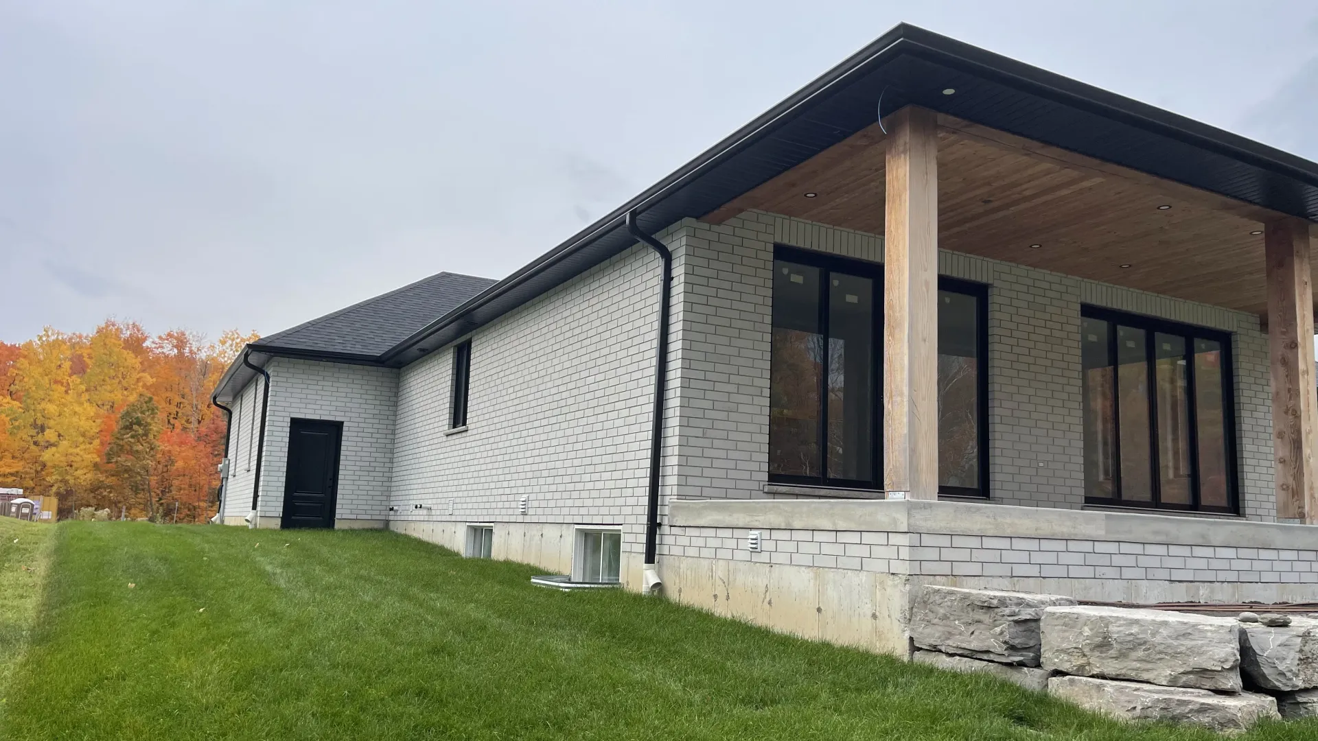 A modern, single-story house under construction with white exterior panels, a dark roof, and a wooden covered porch.