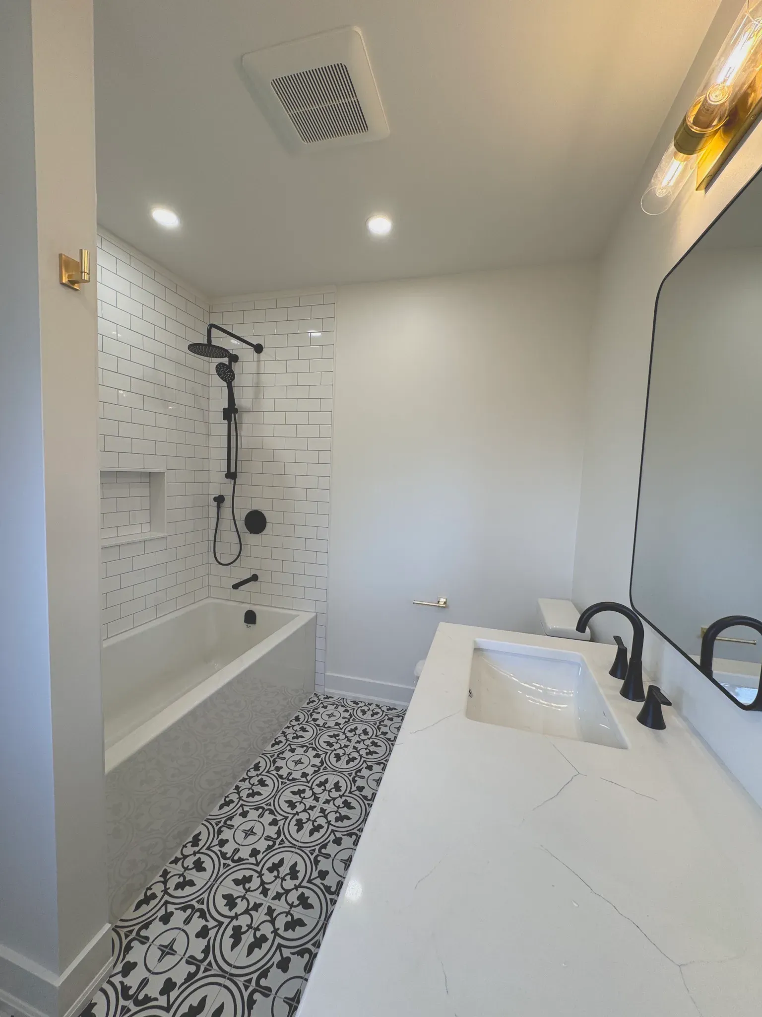 A modern bathroom featuring a white bathtub, black and white patterned tile floor, white wall tile, and a marble vanity.