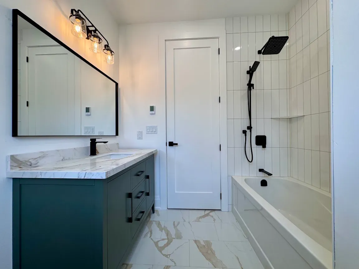 main bathroom with green vanity and vertical subway tile black faucets and mirror