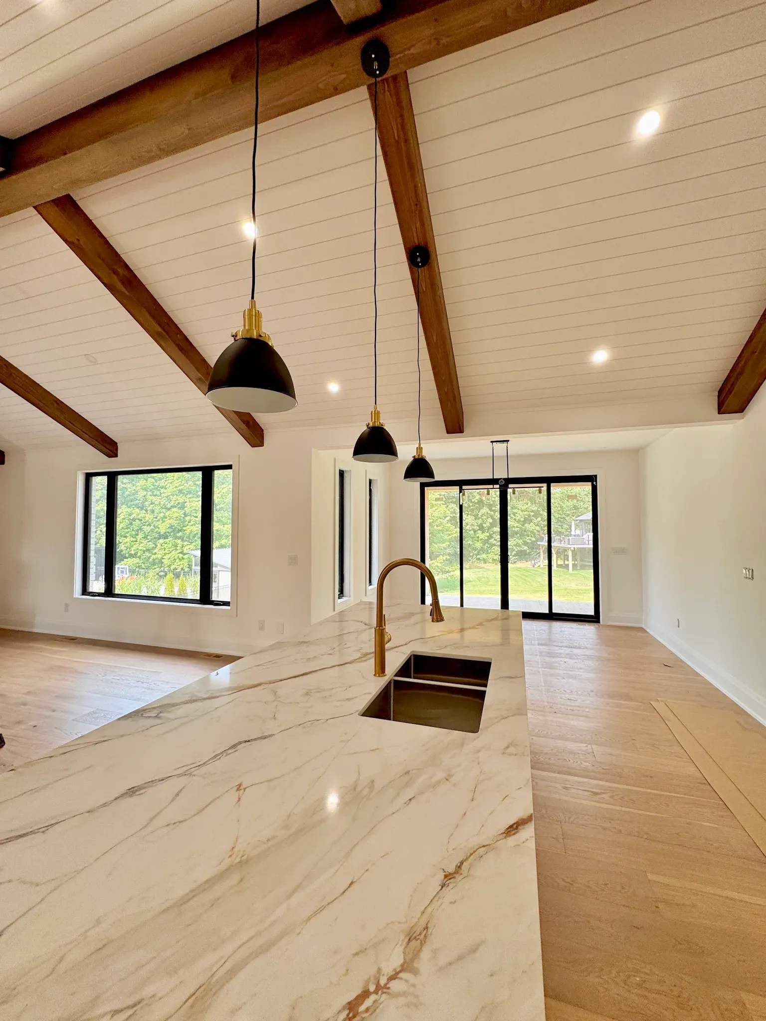Modern kitchen interior with a marble island, dark pendant lights, vaulted wood-beamed ceiling, and sliding glass doors.