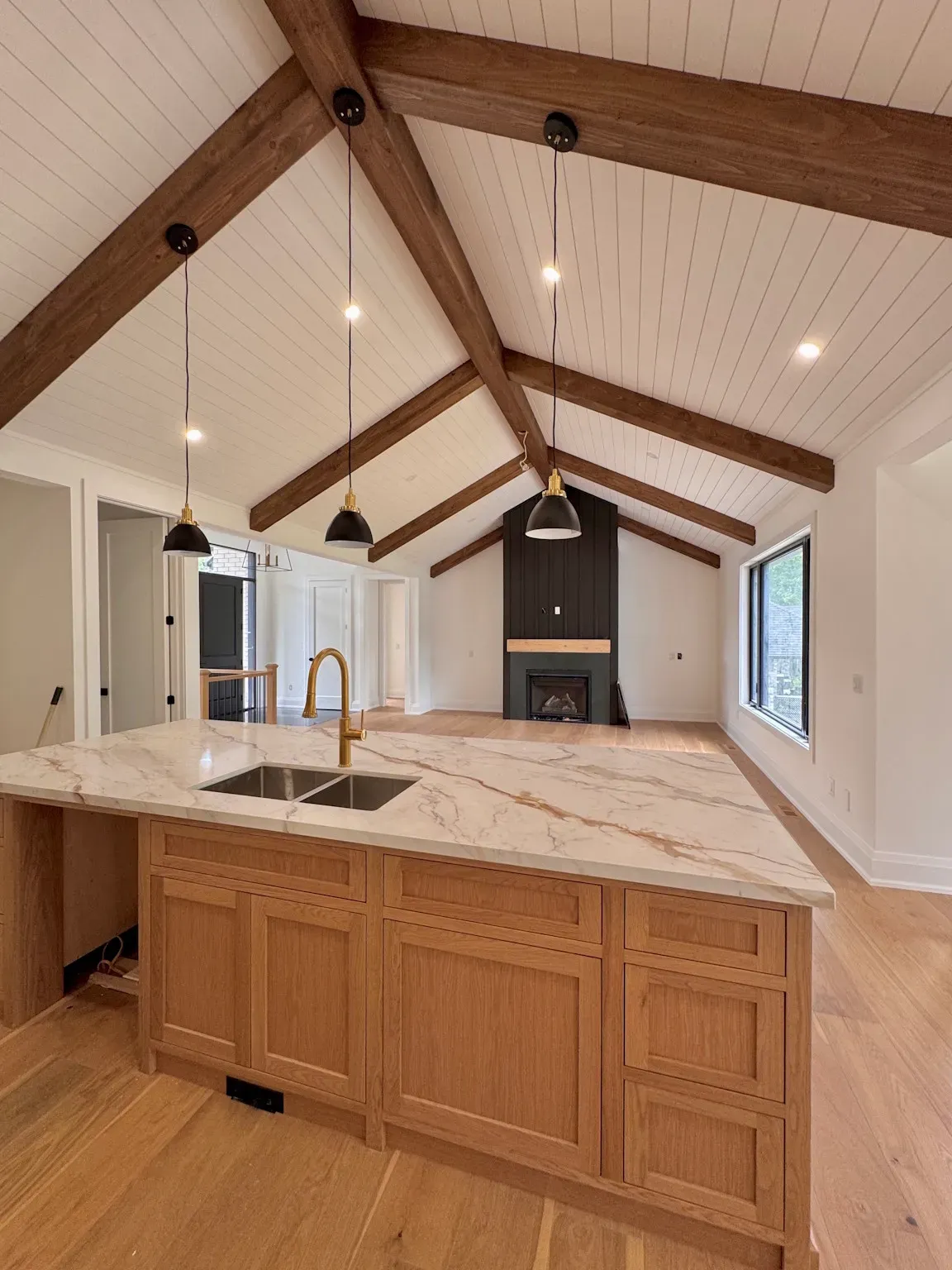 Modern kitchen with wood-beamed vaulted ceiling, marble island, pendant lights, and fireplace focal point