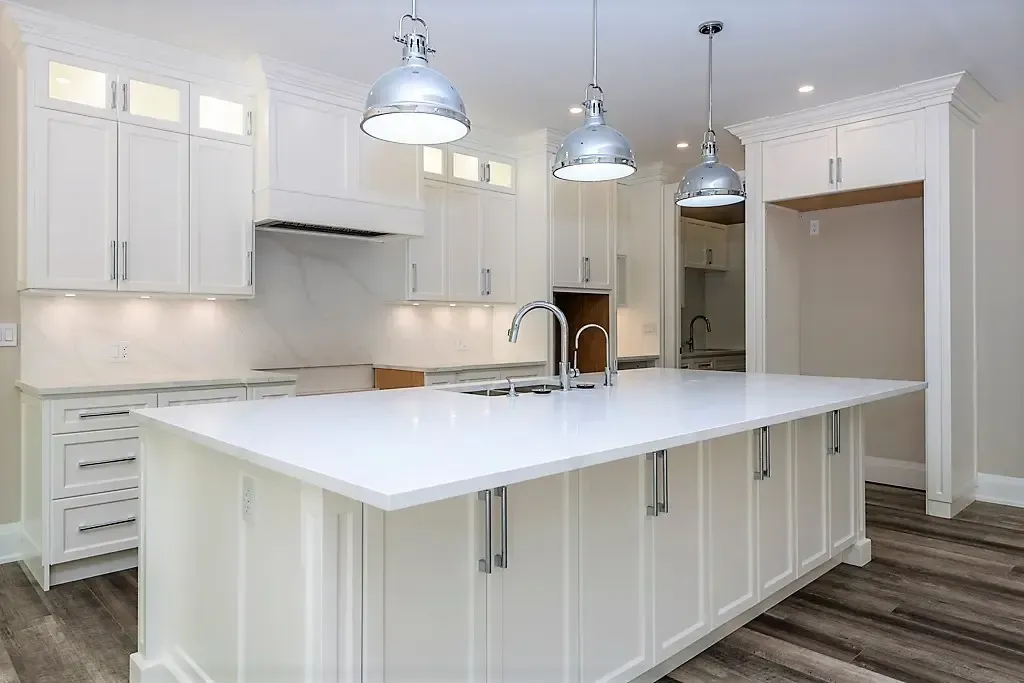 A modern, well-lit kitchen with white shaker cabinets, a large island with a quartz countertop, and three dome lights.