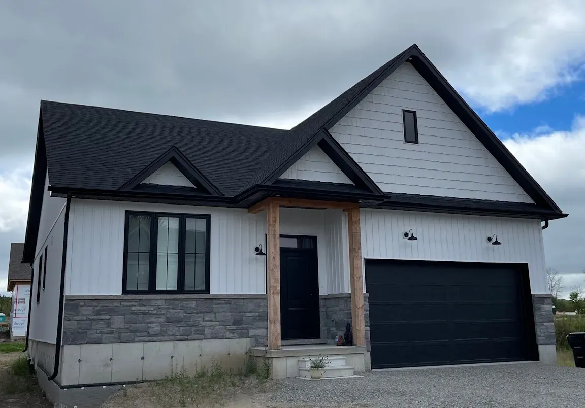 A single-story suburban house with white vertical siding, grey stone base, black roof, and a two-car garage.