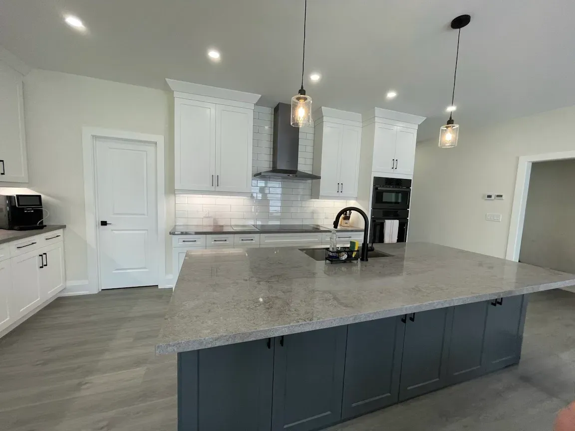 A modern kitchen with white upper cabinets, a large gray island with a granite countertop, and two pendant lights.