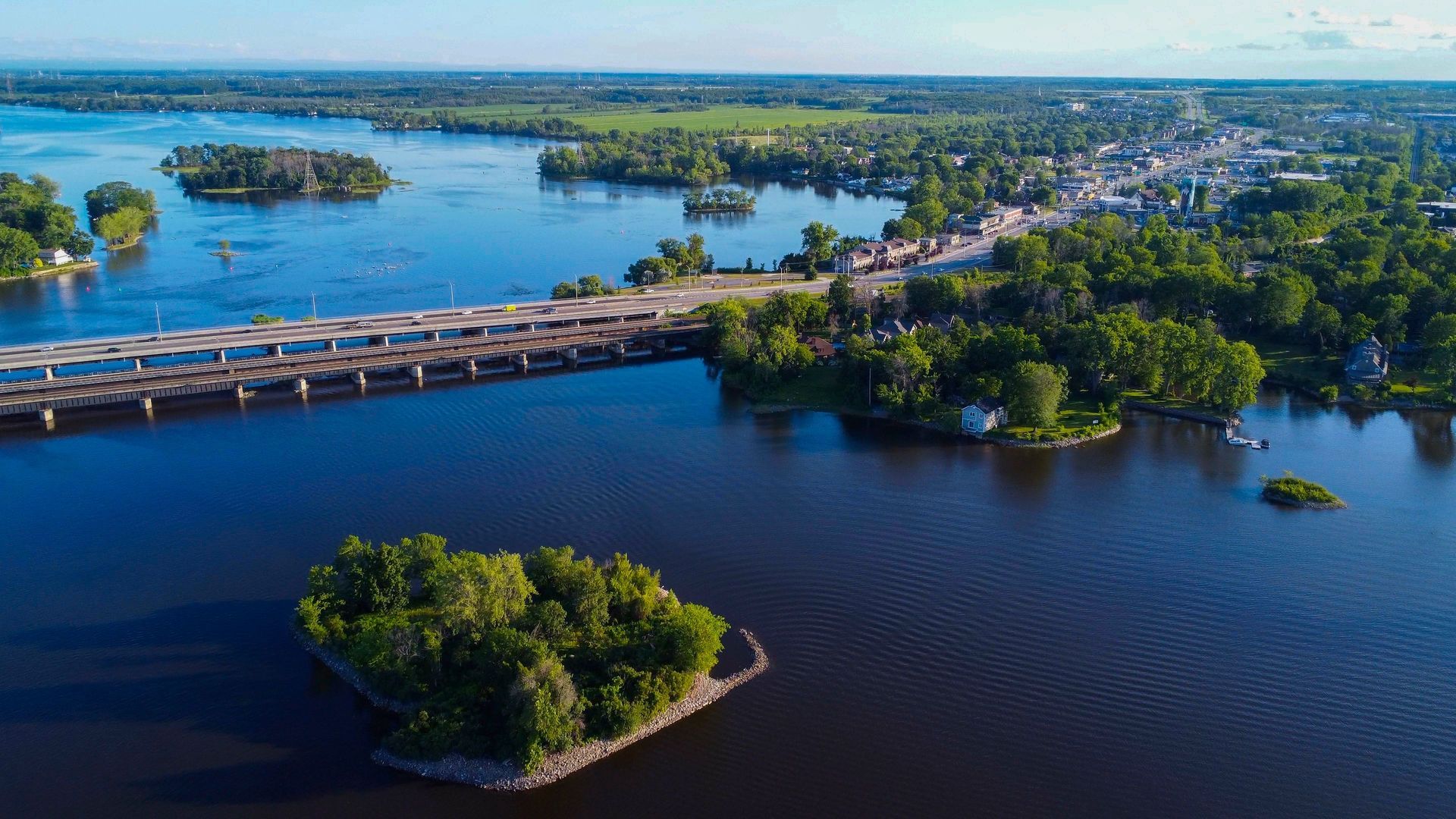 Aerial view of a long bridge over dark blue water near green islands and a distant shoreline