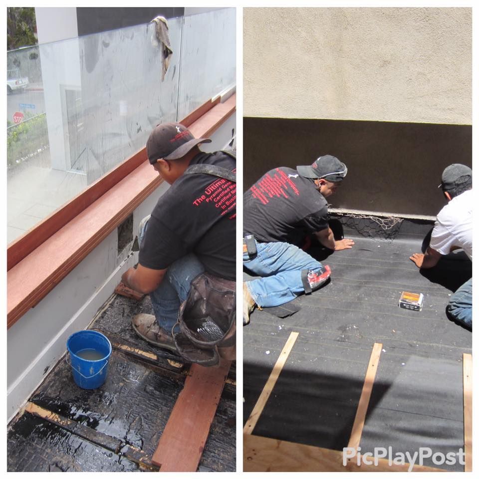 Two workers are repairing a flat roof; one kneels, the other stands.