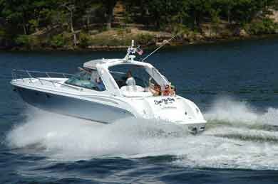 White motorboat speeding across blue water, with passengers aboard. Trees and shore in the background.