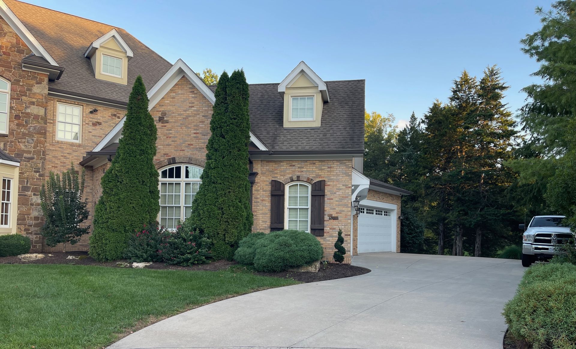 Brick suburban house with ivy, manicured shrubs, and a curved driveway leading to a garage