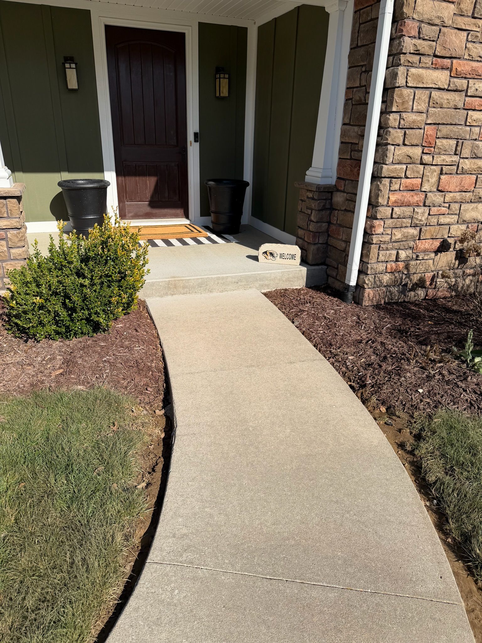 Curved concrete walkway leading to a front porch with brick siding and potted plants.