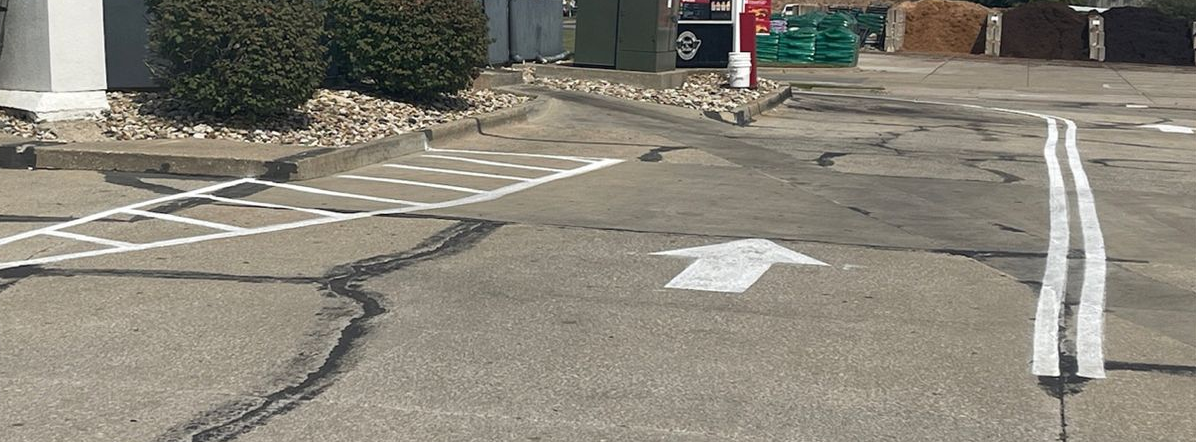Empty parking lot with white directional arrows and cracked pavement near a building entrance