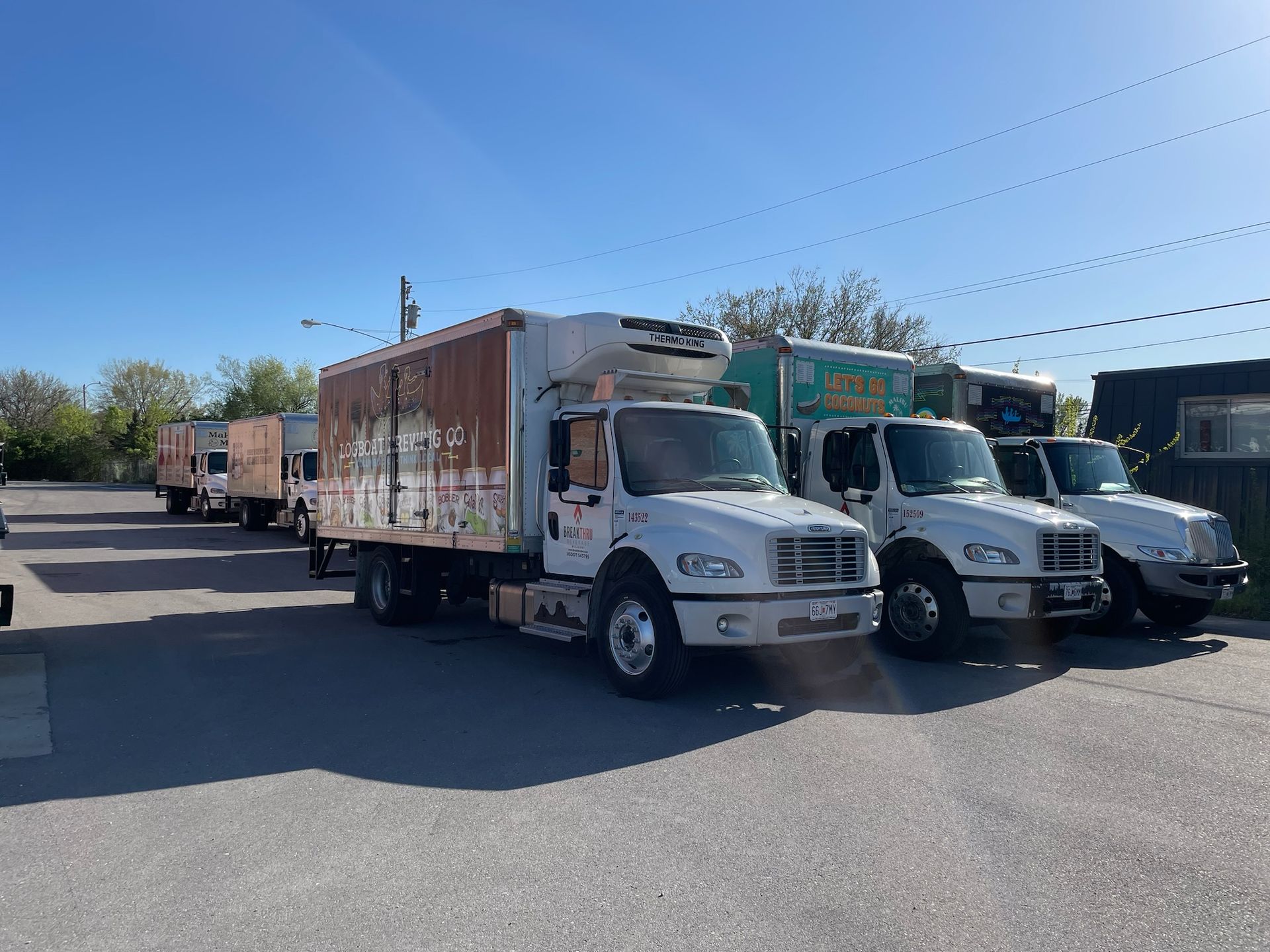Several white delivery trucks parked in a sunny lot, with a large box truck in front