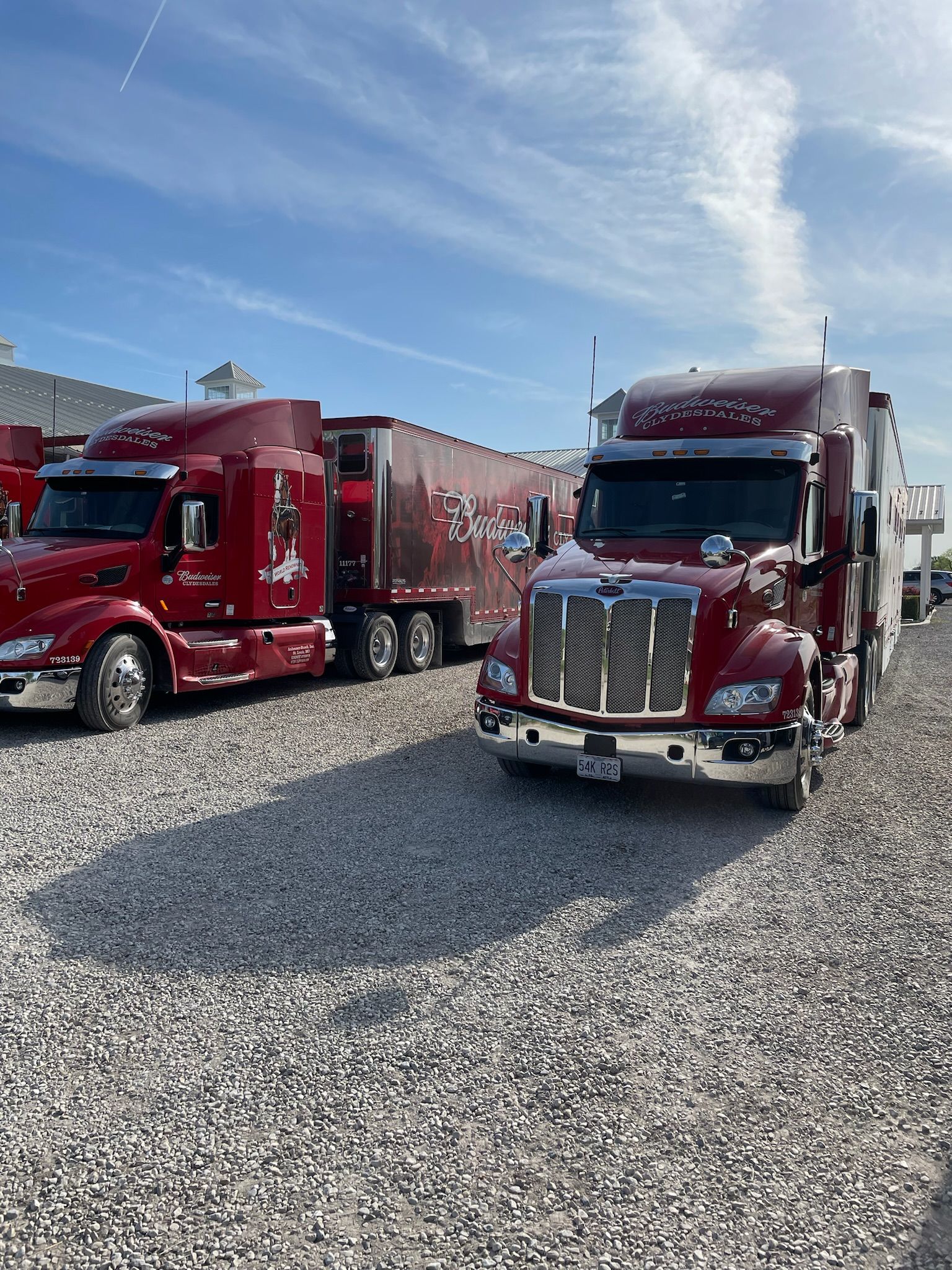 Two maroon semi trucks parked on gravel under a blue sky.