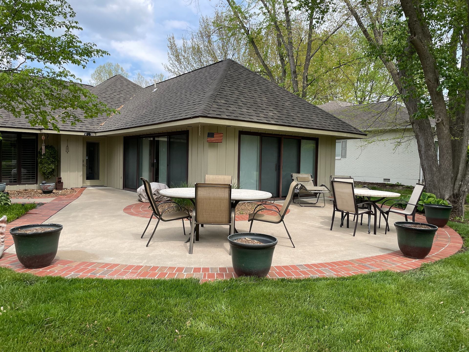 Backyard patio with outdoor tables and chairs beside a tan house under trees