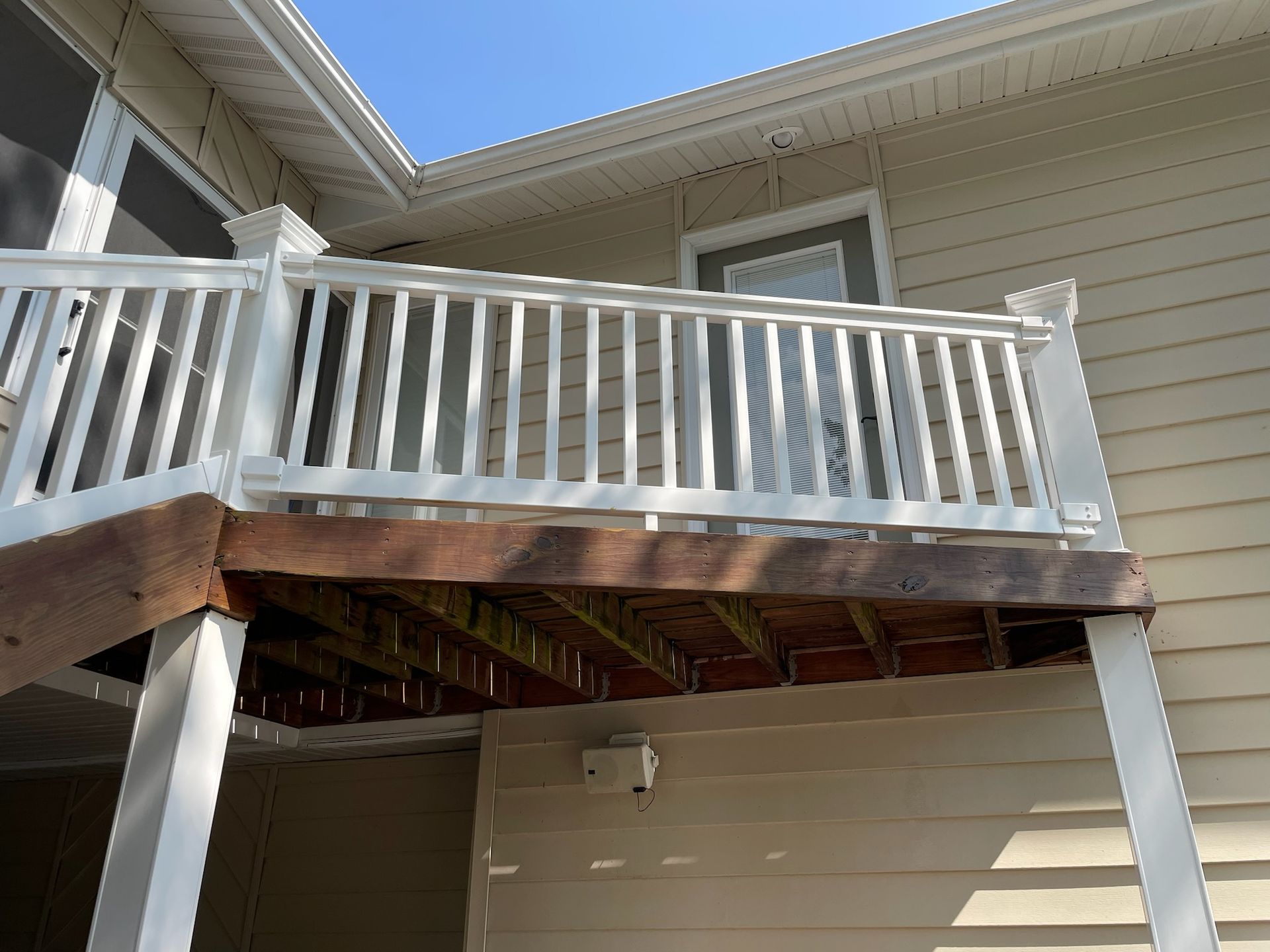 White-railed wooden deck attached to a beige house, viewed from below.