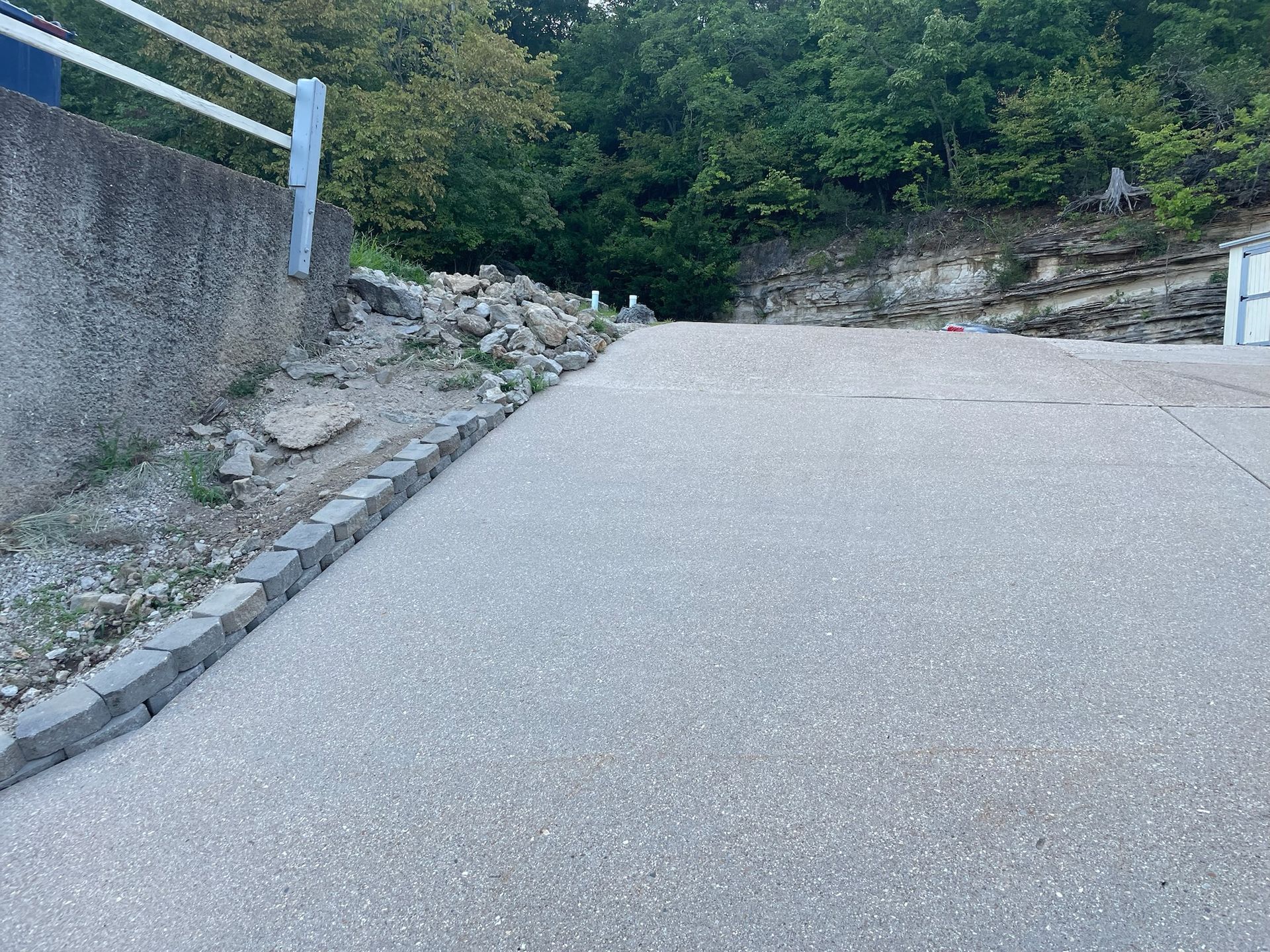 Steep concrete driveway beside a rocky embankment and trees
