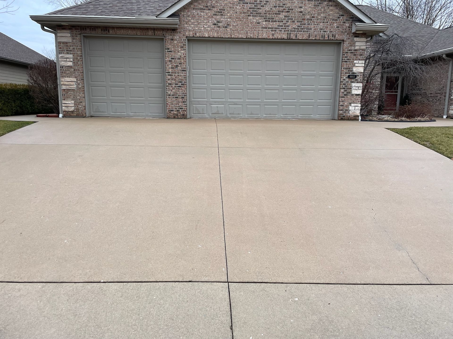 Suburban house with two garage doors and a wide concrete driveway.