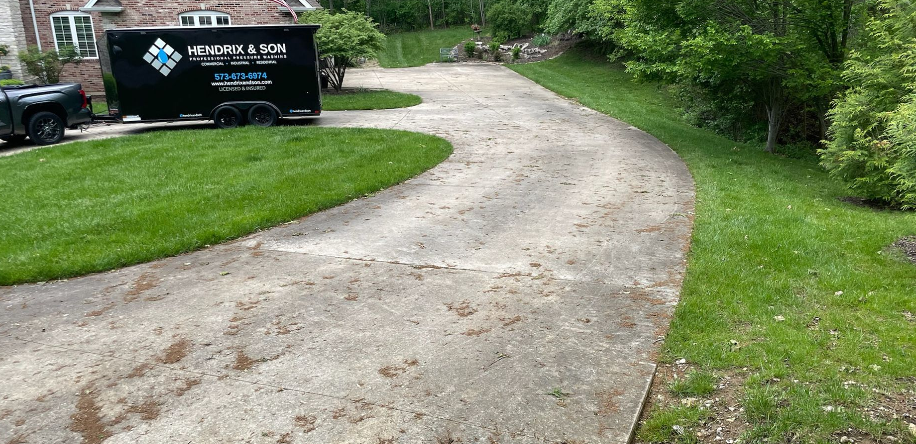 Curved concrete driveway beside a black sign and lush green trees.