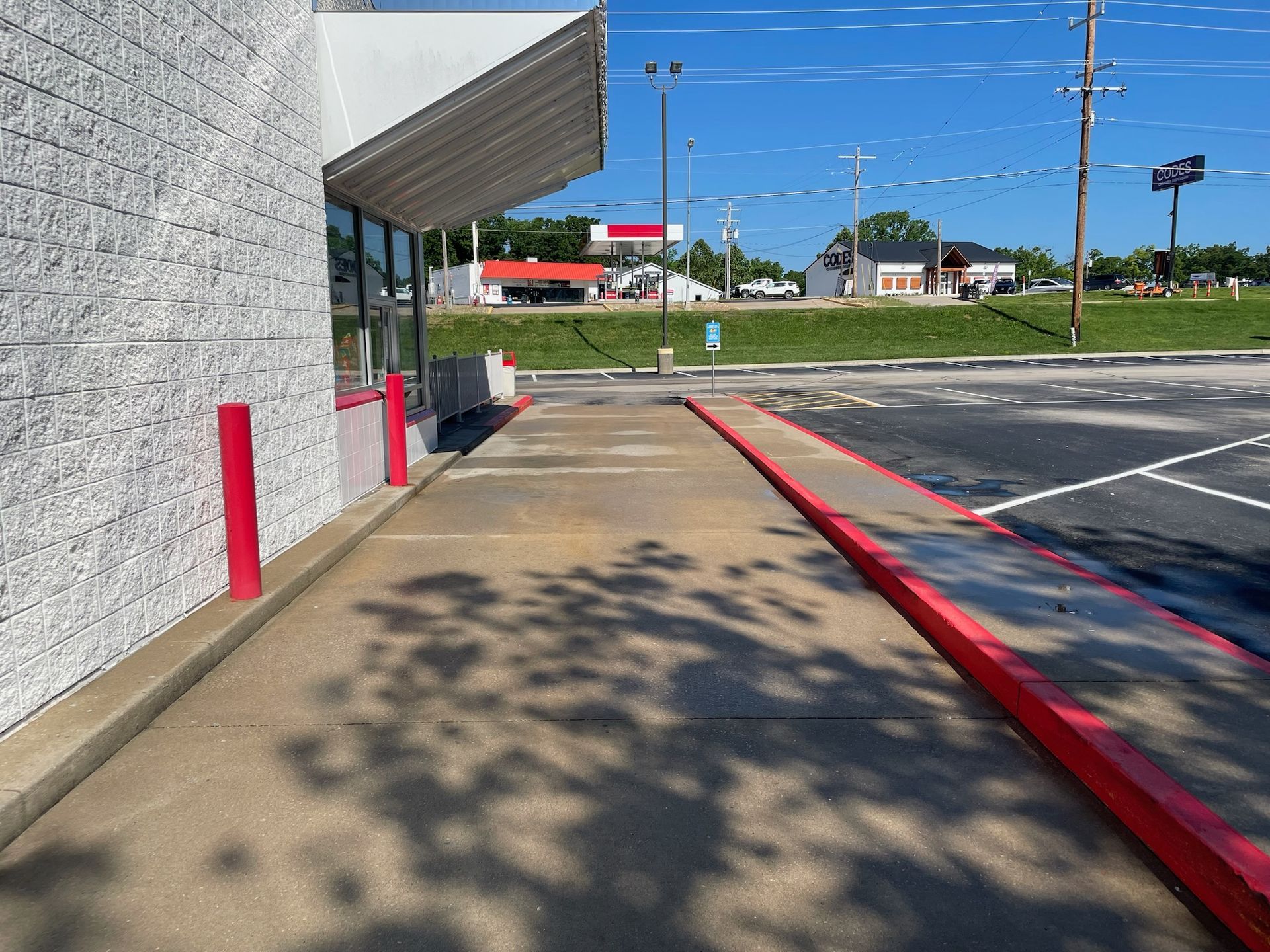 Empty sidewalk beside a building and parking lot, with red curb and awning on a sunny day