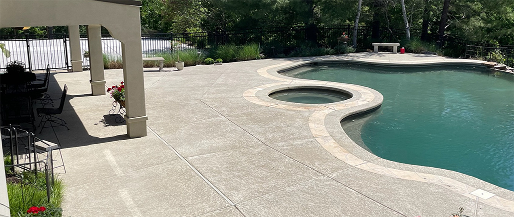 Curved backyard swimming pool with stone deck and shaded patio area
