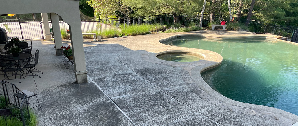 Patio beside a curved turquoise swimming pool with a stone edge and shaded seating area