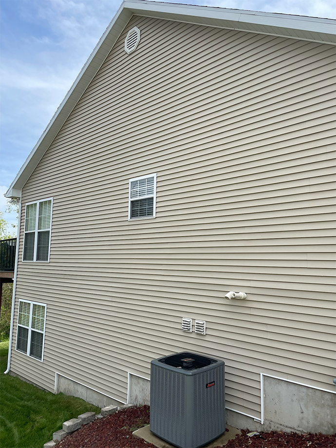 Side view of beige vinyl house with white-trimmed windows and an air conditioner unit on the lawn.