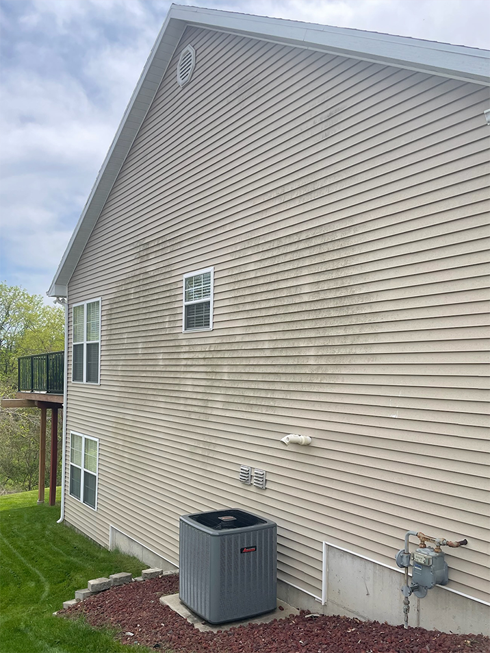 Side view of a beige house with vinyl siding, small windows, utility meter, and an air conditioner unit in the yard