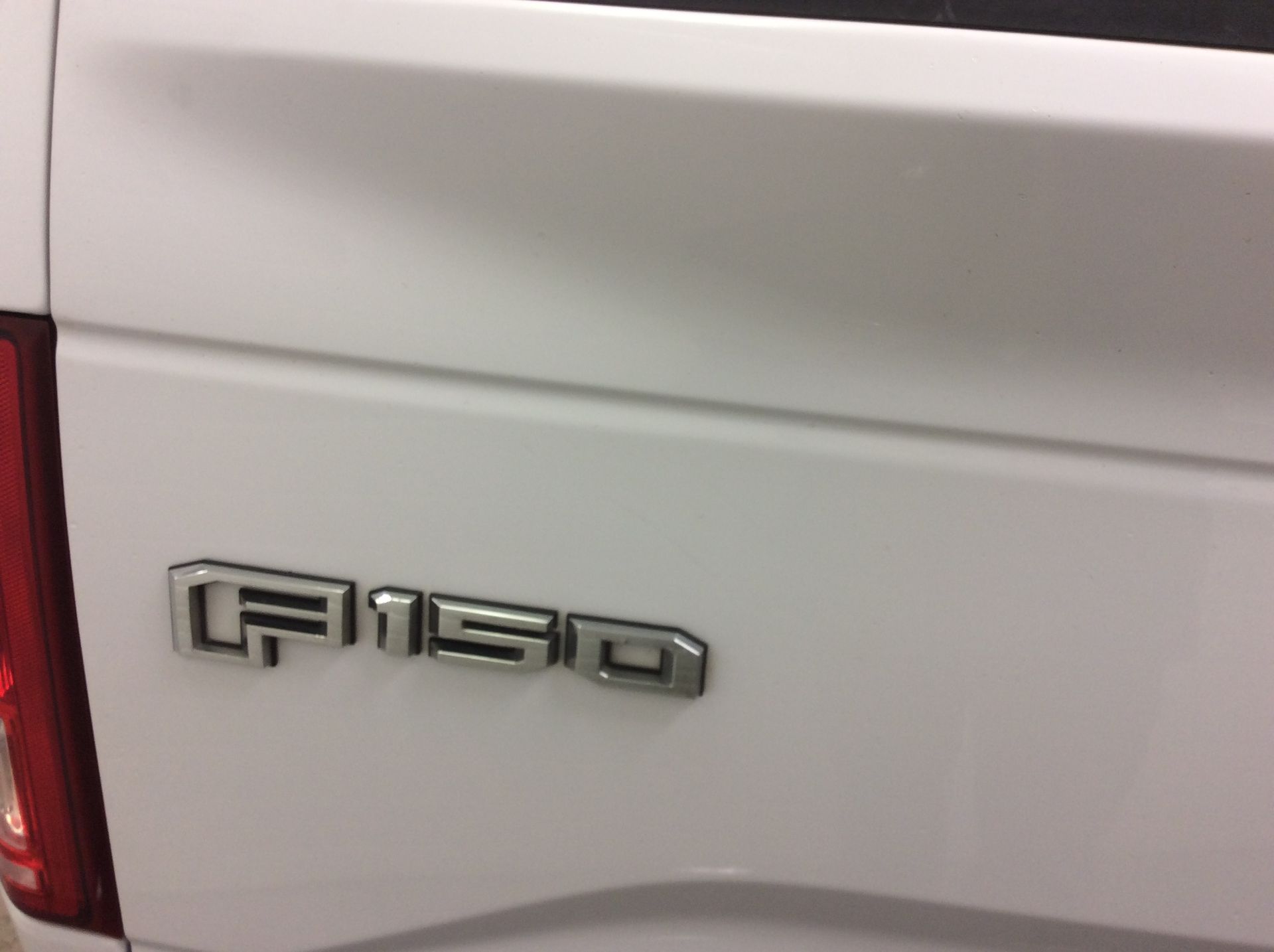 The back of a white ford f150 truck with a damaged tailgate.