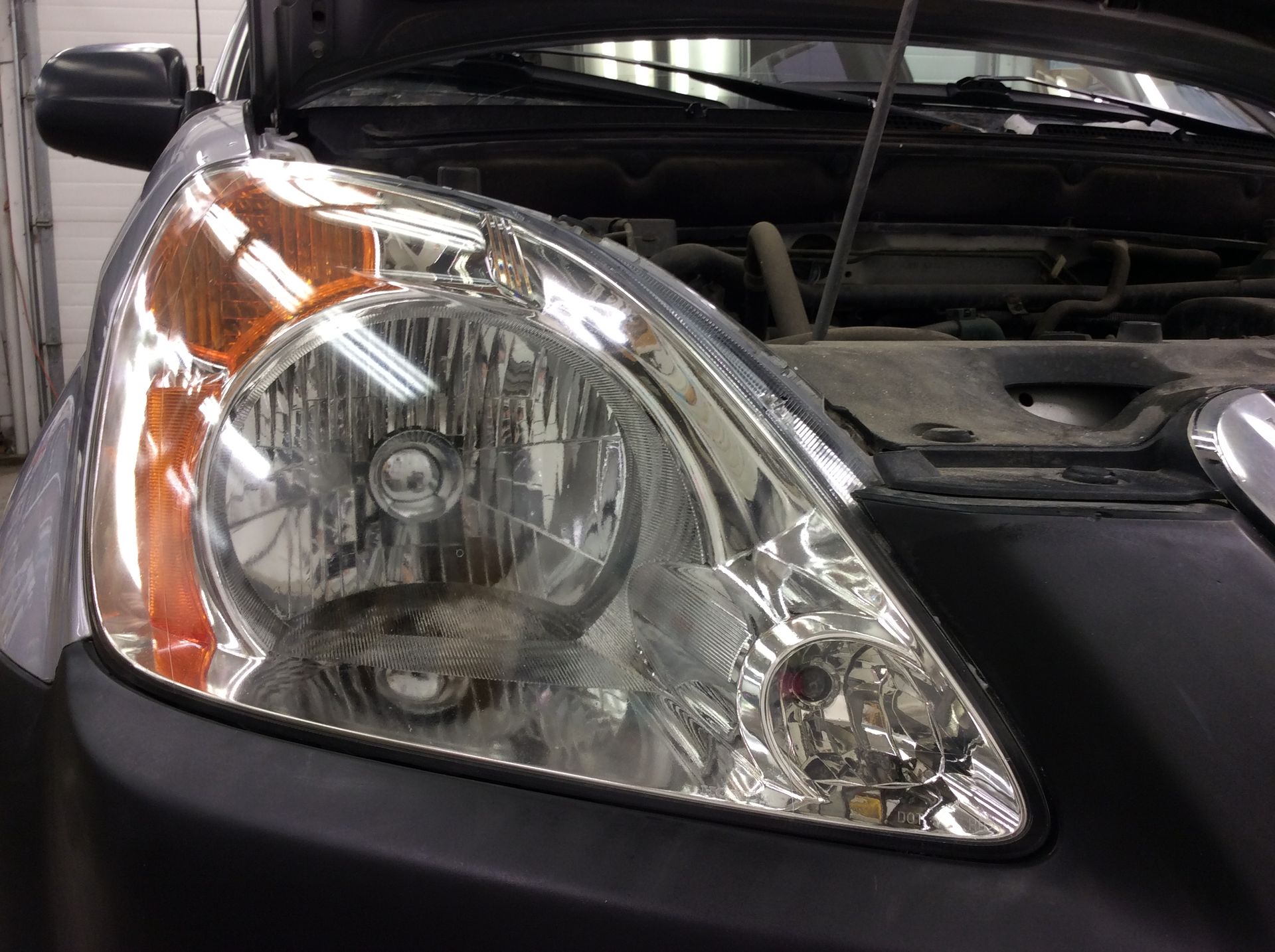 A close up of a car headlight with the hood open.