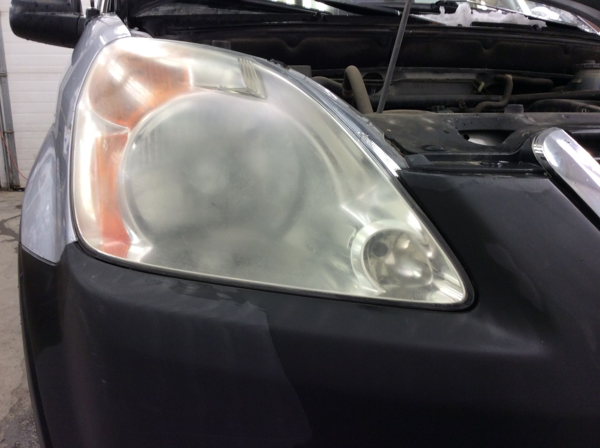 A close up of a car 's headlight with the hood open.