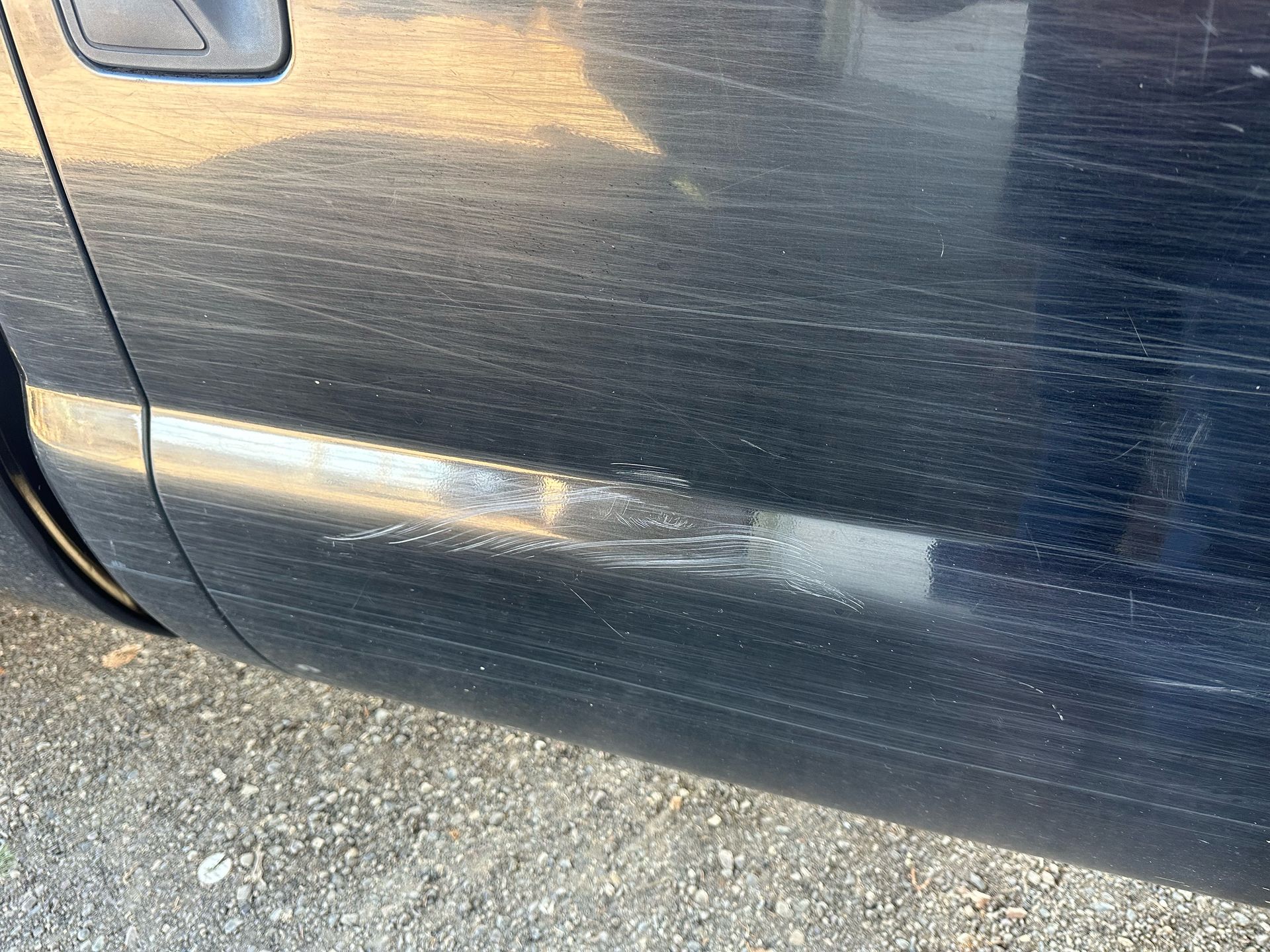 A close up of a car door with a scratch on it.