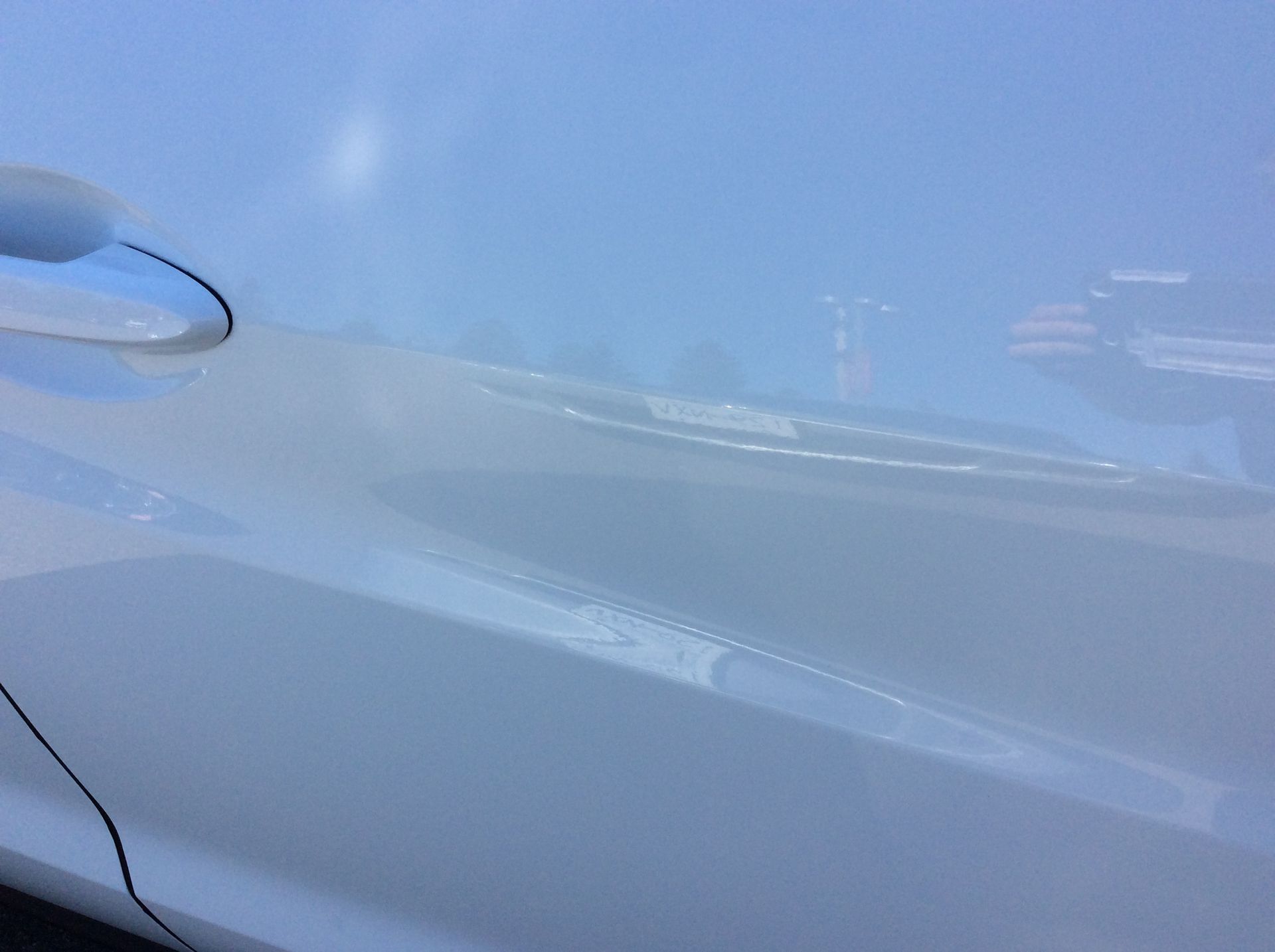 A close up of a white car door with a blue sky in the background.