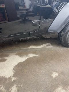A jeep is parked in a garage with a puddle of water on the floor.