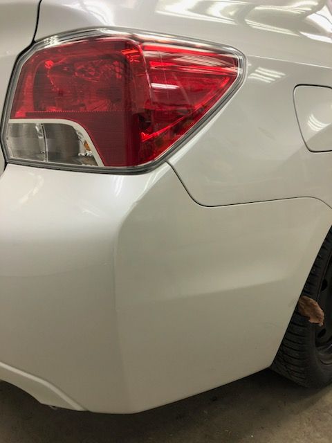 A white car with a red tail light is parked in a garage.