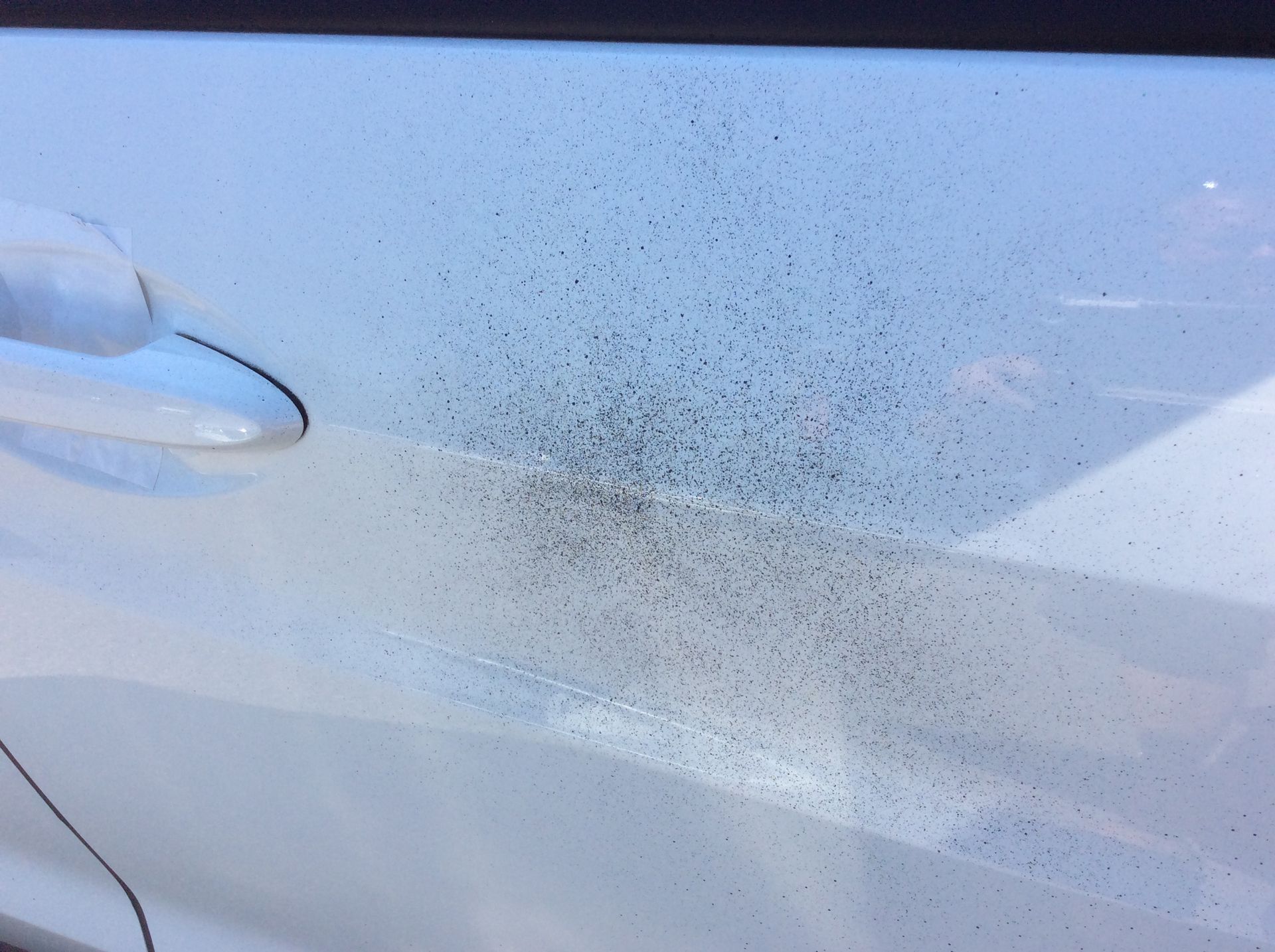 A close up of a white car door with black spots on it