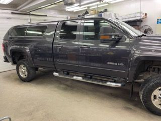 A gray truck with a canopy is parked in a garage.