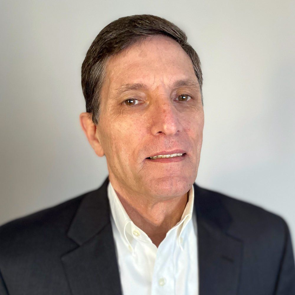 A man in a suit and white shirt is smiling for the camera.