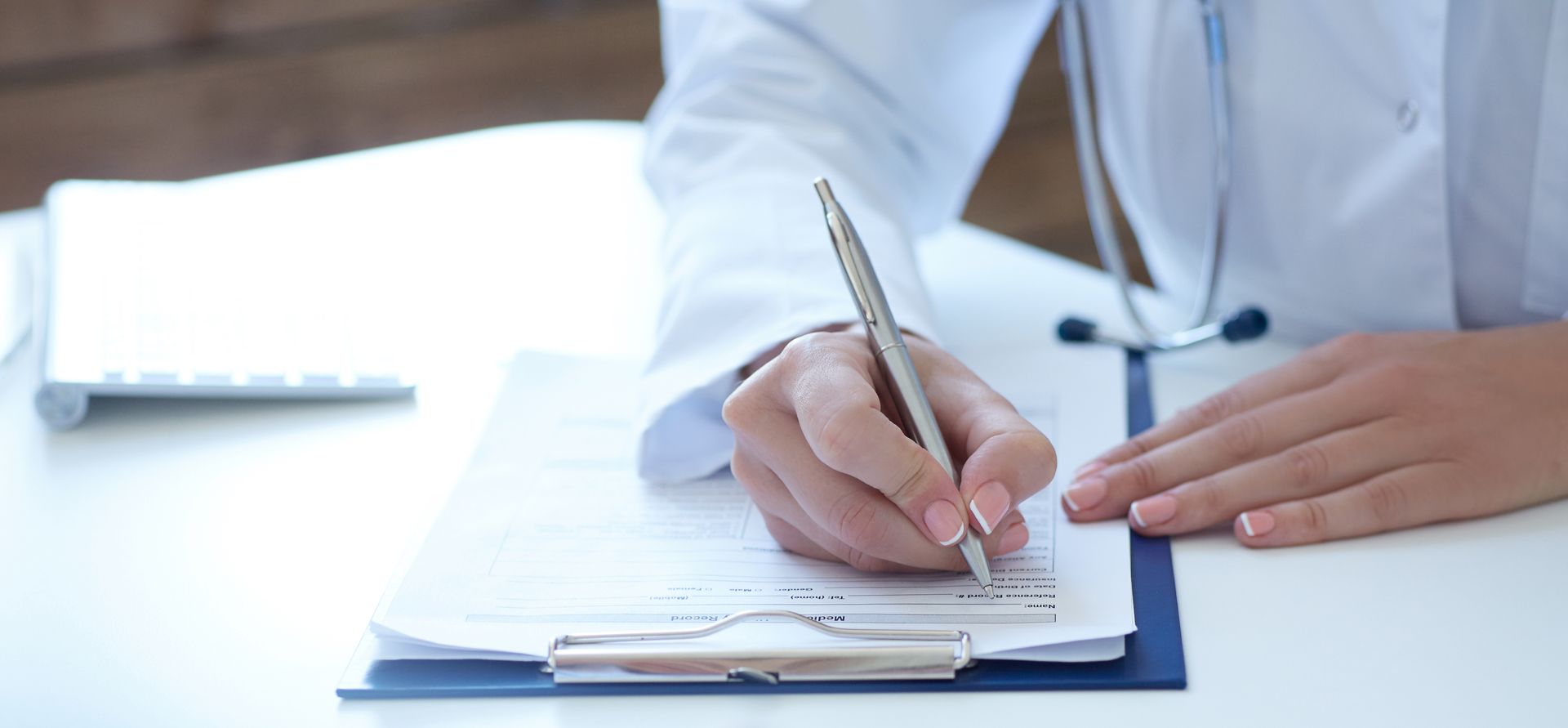 A doctor is writing on a clipboard with a pen.