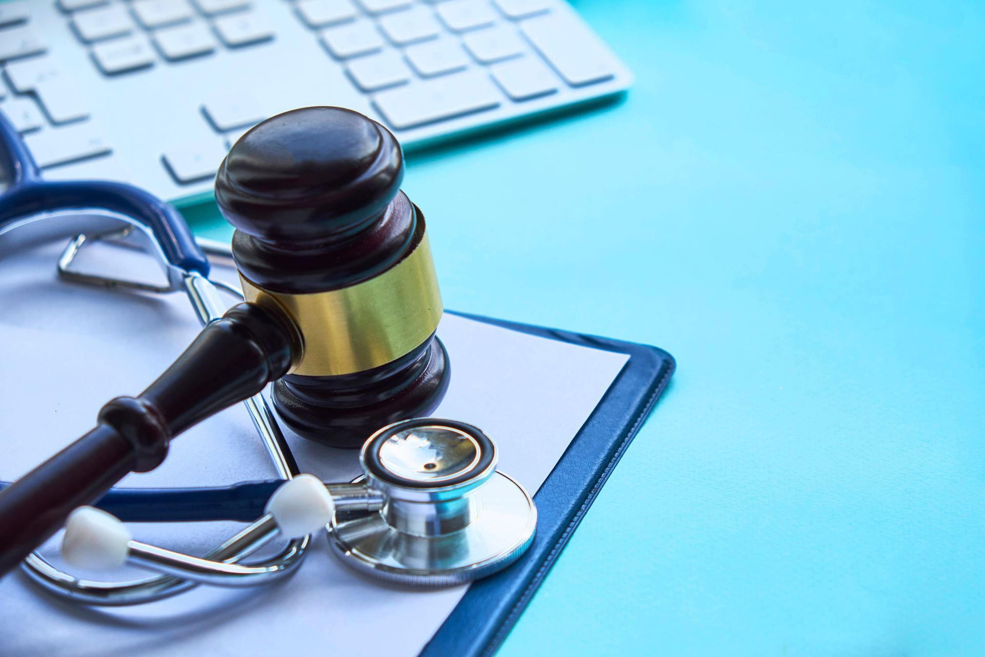 A judge 's gavel and stethoscope are on a clipboard next to a keyboard.