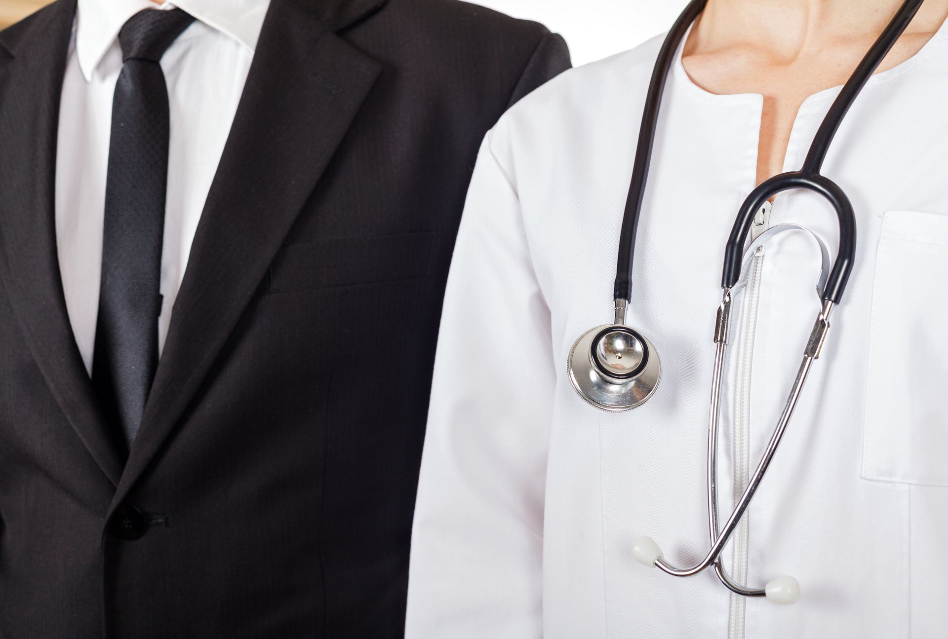 A man in a suit and tie and a woman in a lab coat with a stethoscope around her neck.