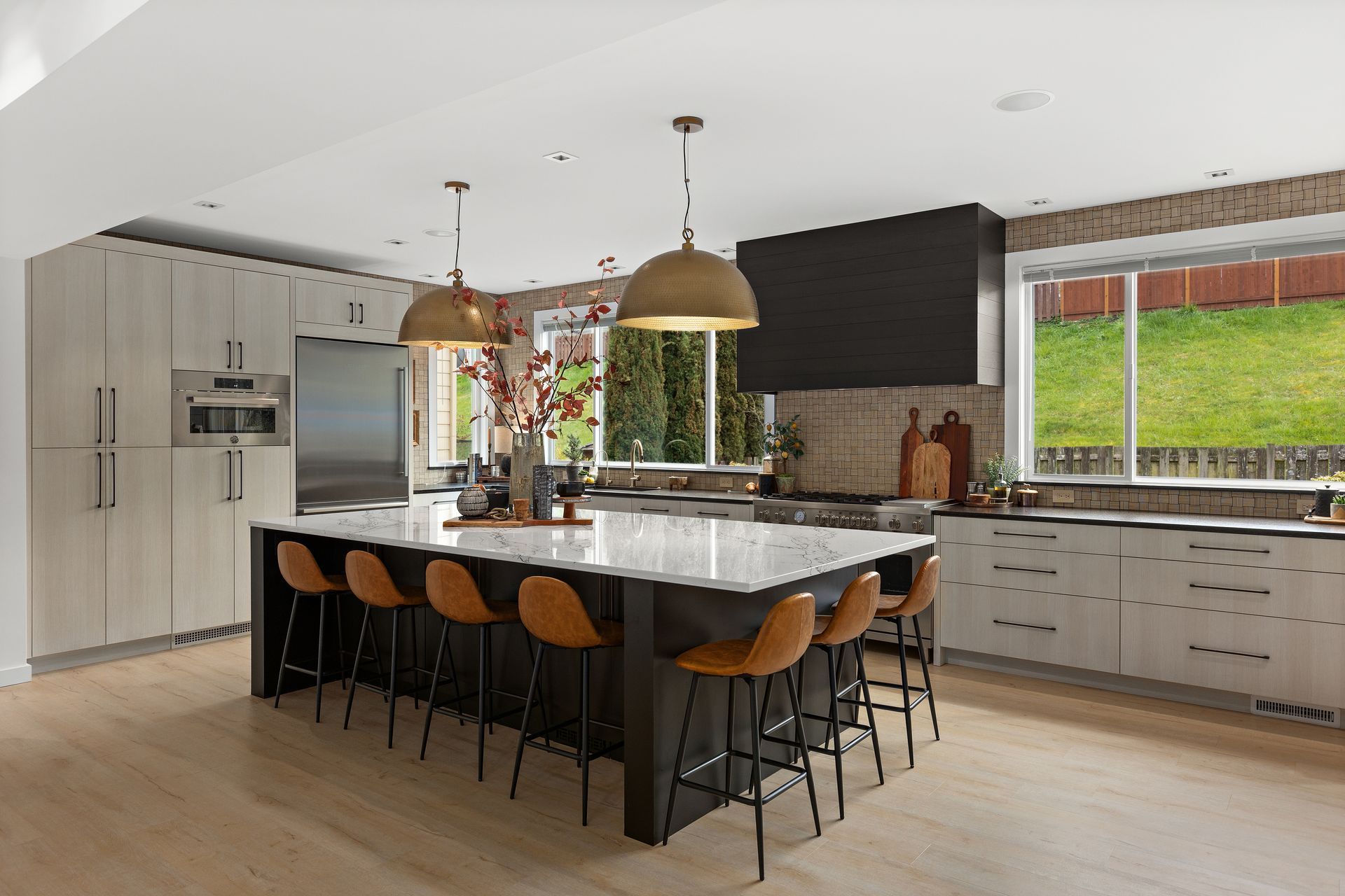 Modern kitchen with island, wooden stools, pendant lights, white cabinets, and large windows