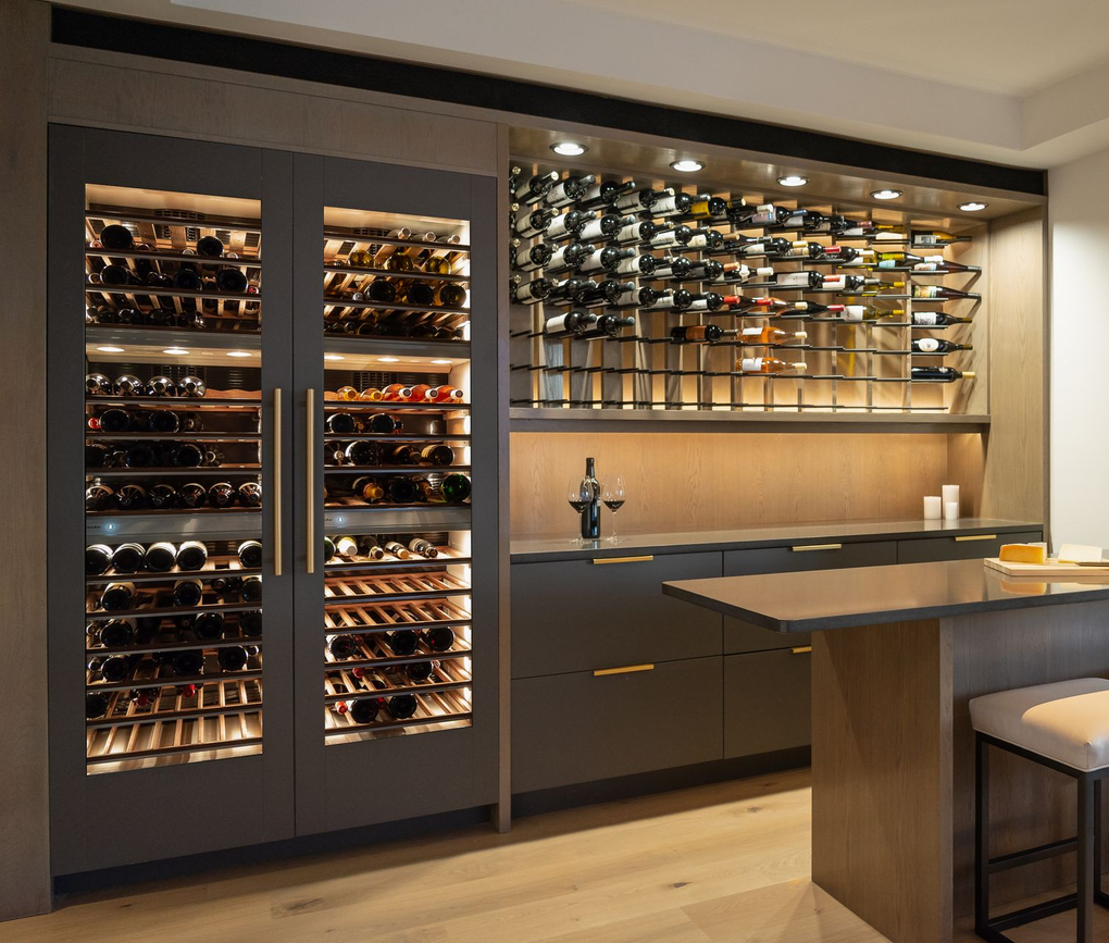 Modern kitchen with built-in wine racks, dark cabinets, and a wood island under warm lighting