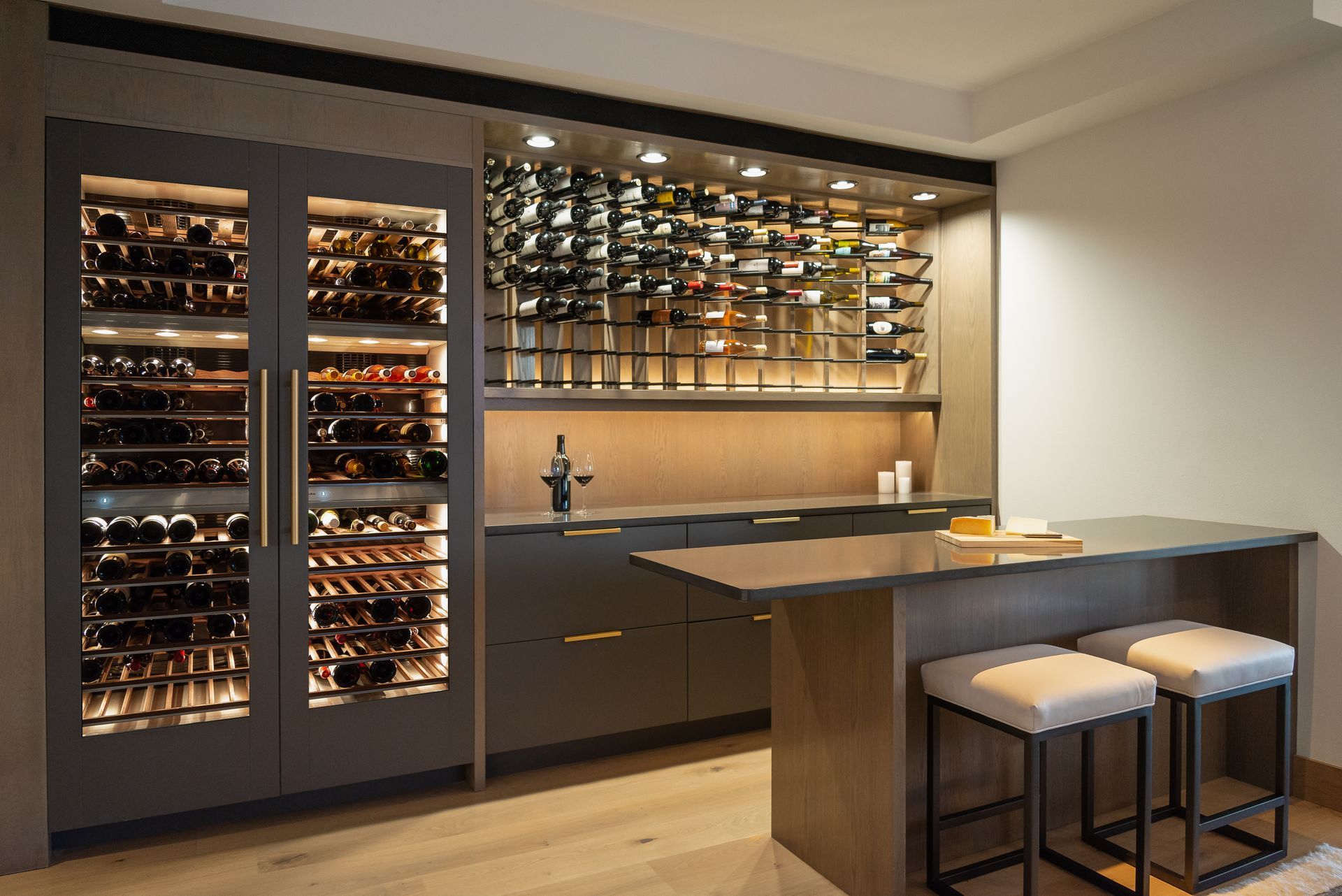 Modern home wine cellar with wall-mounted racks, dark cabinetry, and a small tasting counter with stools