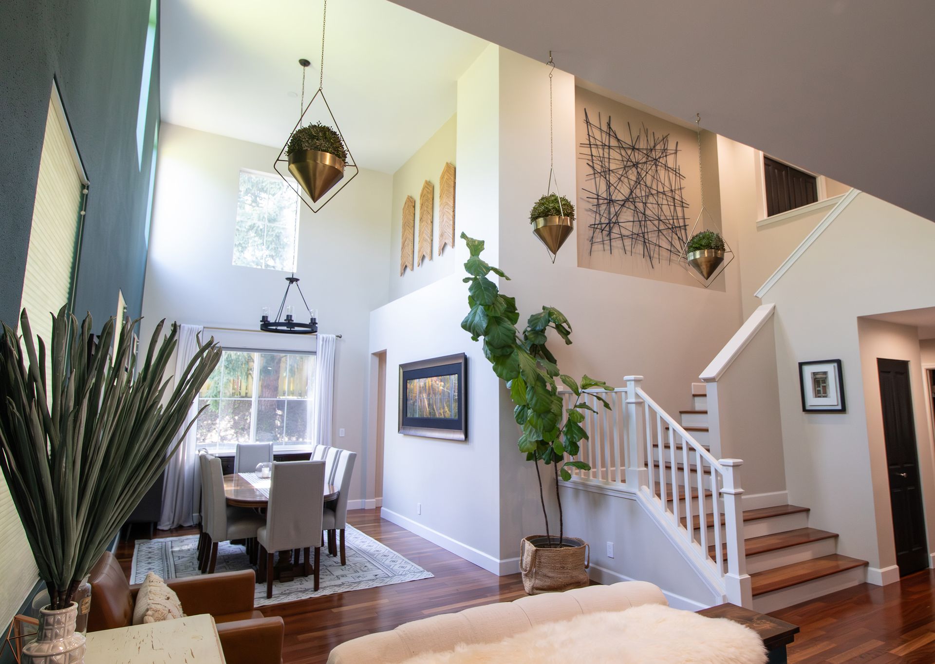 Bright, open foyer with staircase, hanging plants, dining area, and hardwood floors