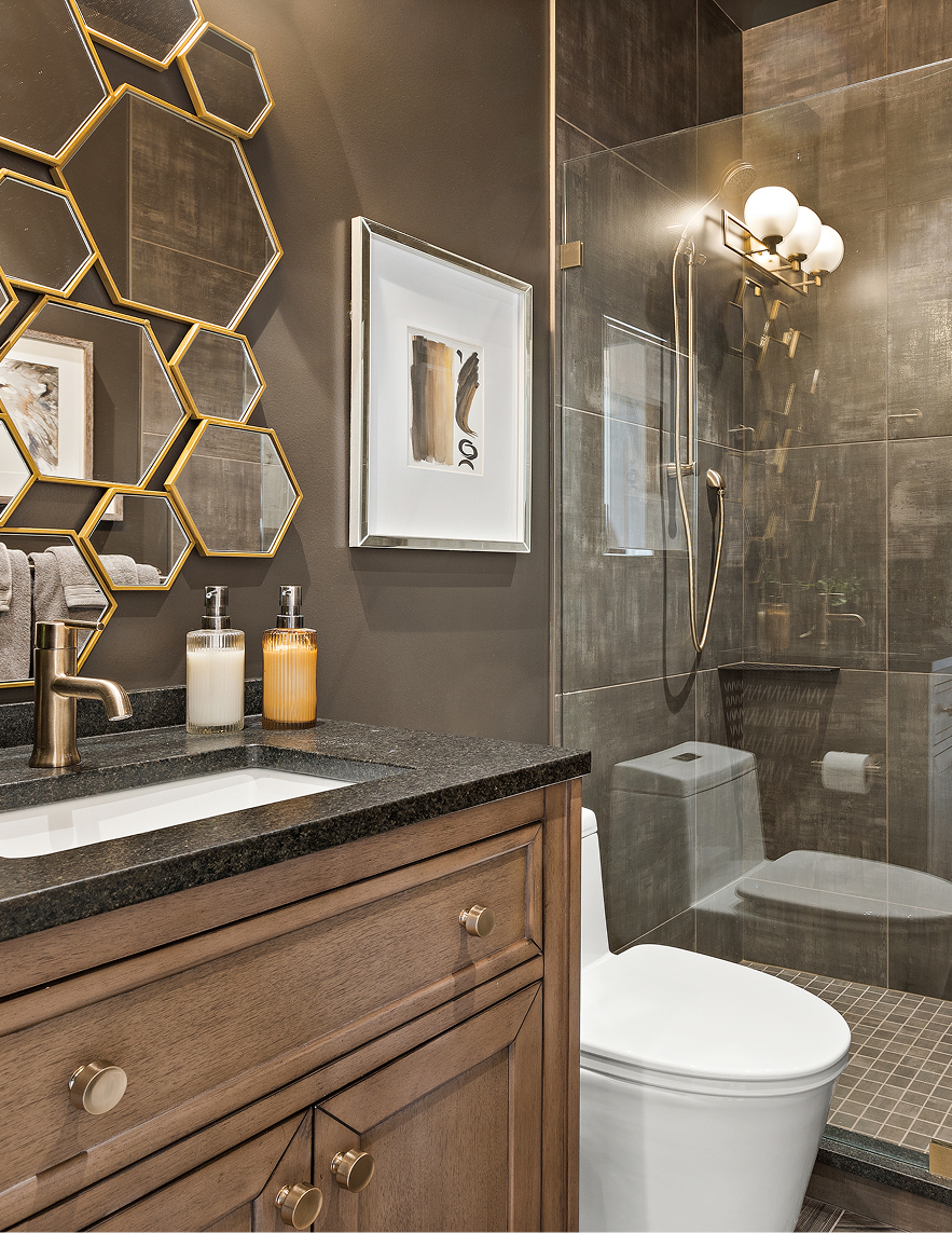 Modern bathroom with dark tile, gold hexagon mirror decor, and a white toilet beside a glass shower.