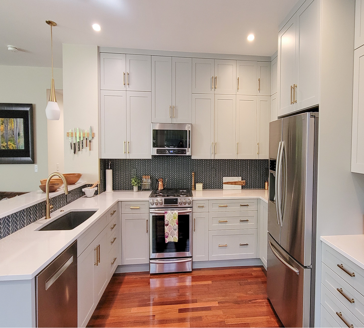 Bright modern kitchen with white cabinets, stainless appliances, black backsplash, and warm wood floors.